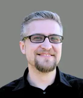 Headshot of Jerad Bitner wearing glasses and black shirt on gray background.