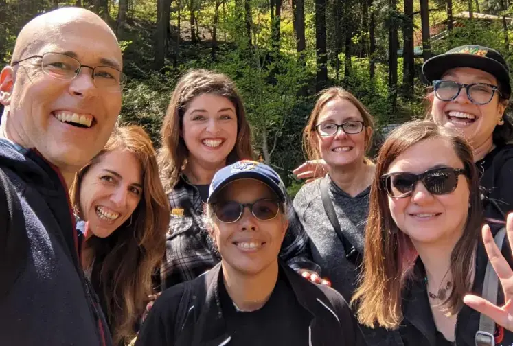 A group of six Lullabot employees gather for a photo in a forest on a sunny day.