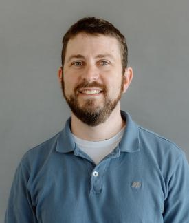 Adam Varn wearing a teal polo shirt in front of a gray background.