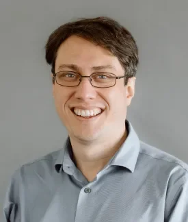 Photo of Andrew Berry, white male wearing a blue button down oxford shirt in front of a gray background.