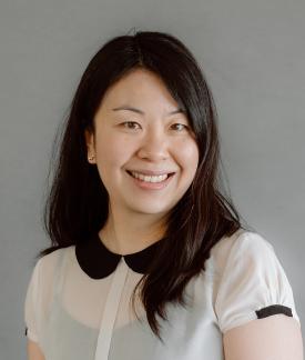 Betty Tran wearing a white blouse with black collar in front of a gray background.