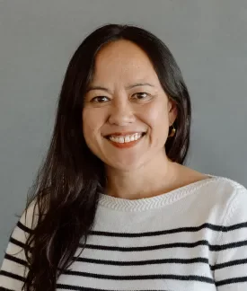 Cat Rude wearing a long-sleeved white sweater with black stripes in front of a gray background.