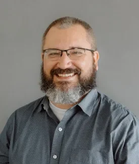 Darren Petersen wearing a blue button down shirt with white polka dots in front of a gray background