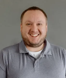 Dave Reid wearing a gray polo shirt in front of a gray background.