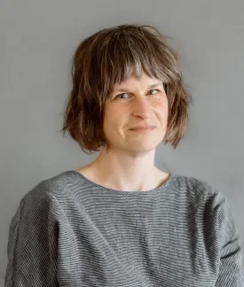 Frances Duncan wearing a black and white striped top in front of a gray backgound.