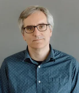 Greg Dunlap wearing a teal button down shirt in front of a gray background.