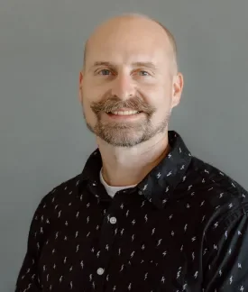 Jared Ponchot wearing a dark button down shirt in front of a gray background.