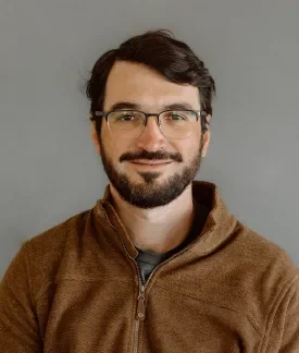 Javier Reartes wearing a brown hoodie in front of a gray background.