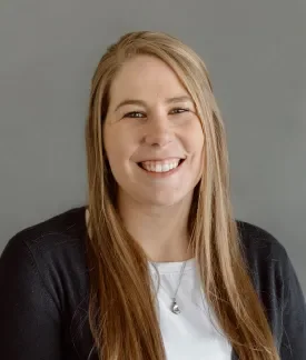 Kayla AhoWalsh wearing a black sweater with white t-shirt in front of a gray background.