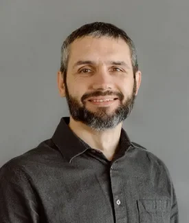 Matt Robison wearing a dark gray button down shirt in front a gray background.