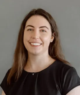 Megh Plunkett wearing a black short-sleeved shirt in front of a gray background.