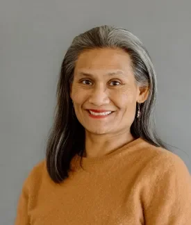 Nikki Flores wearing an orange sweater in front of a gray background.