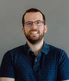 Owen Bush wearing a dark blue polo shirt in front of a gray background.