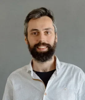 Pablo Lopez Escobes wearing a white button down shirt with a little black dots and a black t-shirt underneath in front of a gray background.