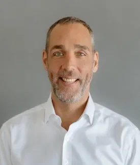 Photo of Seth Brown, white male wearing a white button down oxford shirt in front of a gray background.