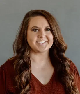 Sydney Barnes in a red v-neck top in front of a gray background.