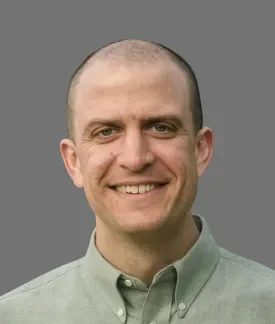 Tim McDorman wearing a light green button down shirt in front of a gray background.