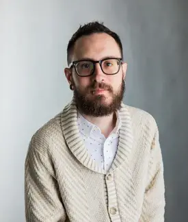 A photograph of Jason Blanda, a 36 year old man with short brown hair, brown eyes, glasses and a tan sweater. 