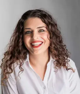 A photograph of Helena McCabe, a 35 year old woman with long brown curly hair, green eyes, and a white collared shirt. 