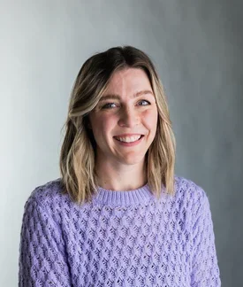 Laura Donelan wearing a purple sweater in front of a gray background.