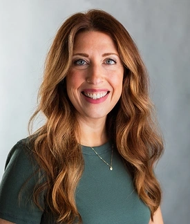 A white woman with red hair, standing in front of a gray background.