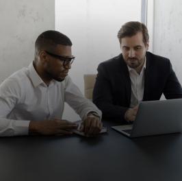 Two people sitting at a table, looking at a computer