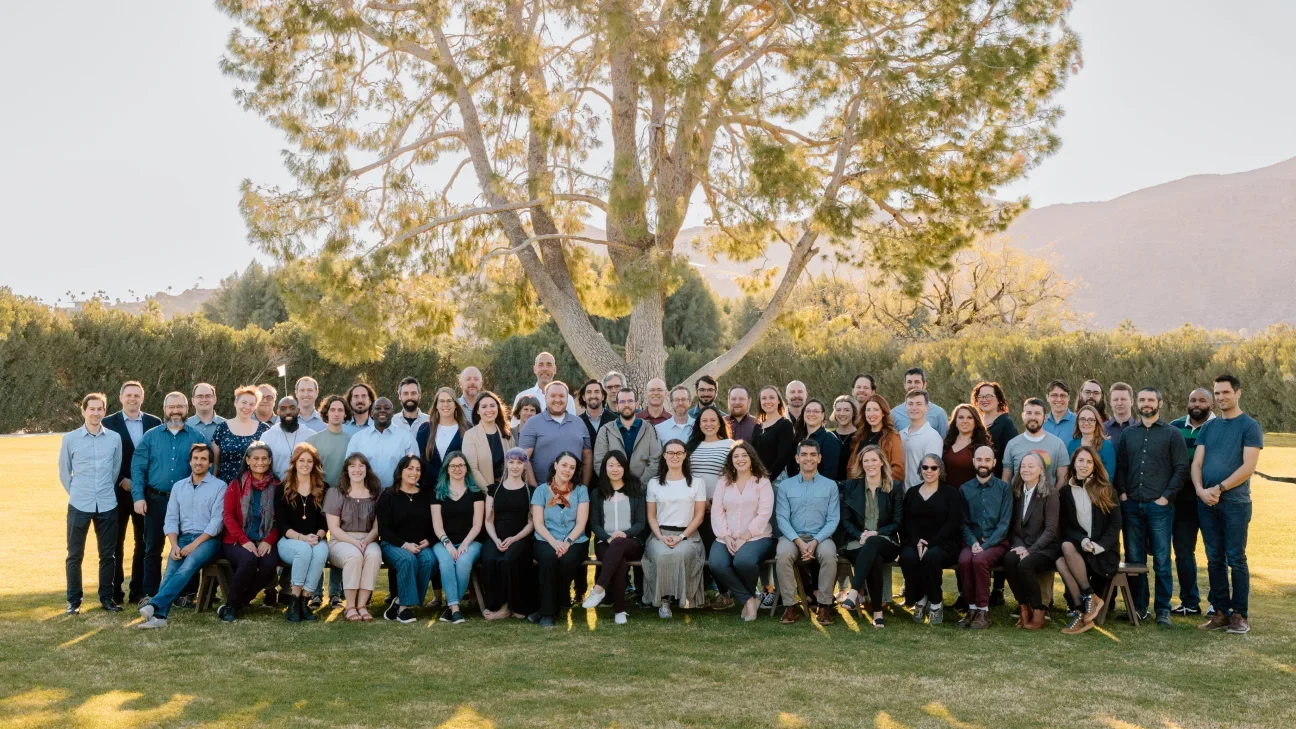 Team photo taken outdoors in the grass with a tree and mountains in the background.