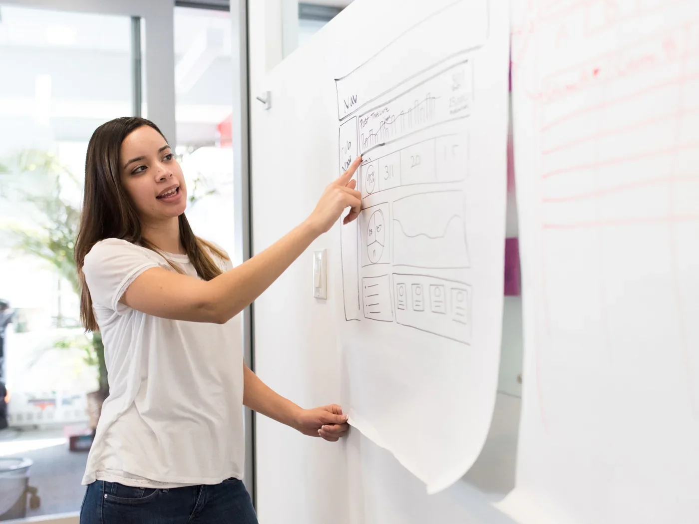 A person points to a piece of paper with illustrations that is hung on a wall.