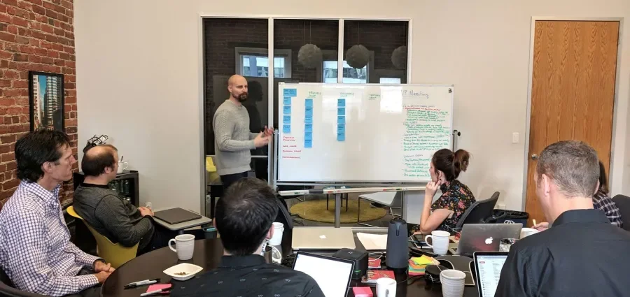 Group of people around a table looking at the facilitator, who is standing