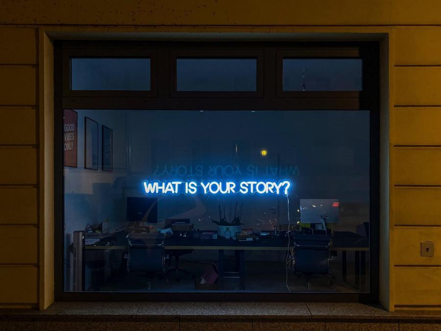 Neon words on a window spelling out "What is your story?"