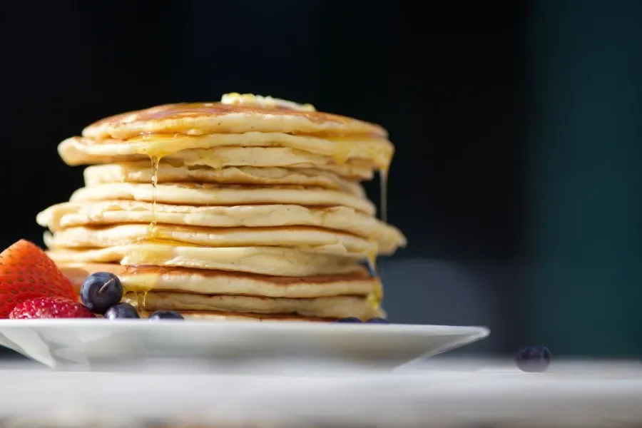 A stack of pancakes made from the Jackson’s Recipe batter, dripping with butter, garnished with strawberries and blueberries.