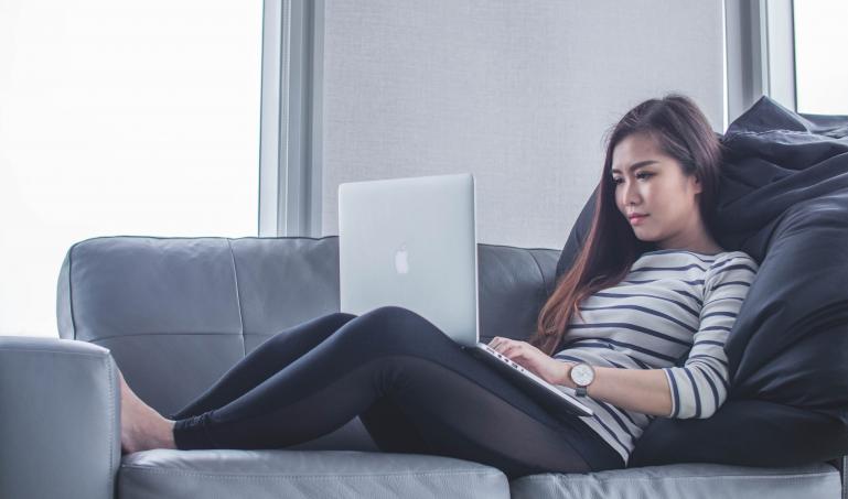 Woman with laptop working on her sofa.