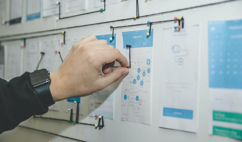 A hand putting a thumbtack onto a board full of mockups