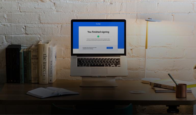 Desk with some books and a laptop displaying the DocuSign completion page that says, "You finished signing."