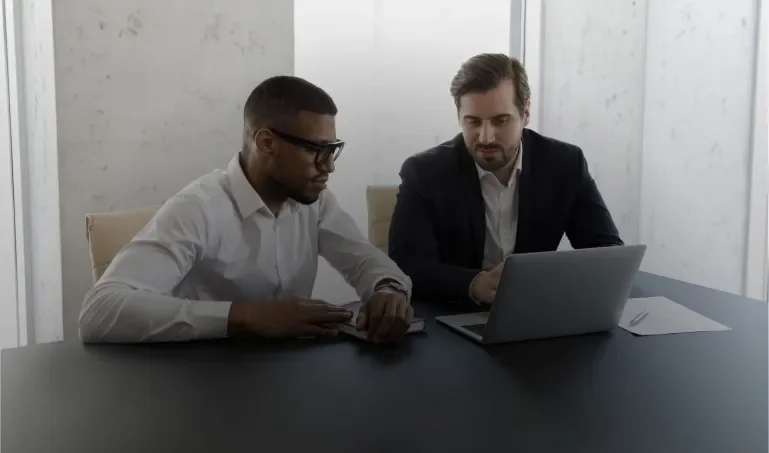 Two people sitting at a table, looking at a computer