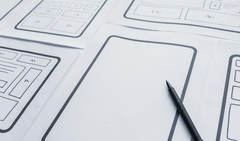A pen laying on top of wireframes drawn on white paper