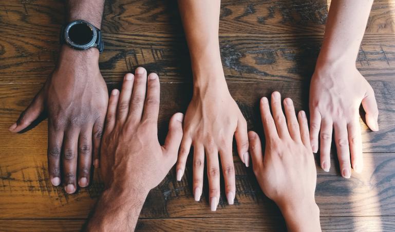 Several hands interlocked on top of a wooden table