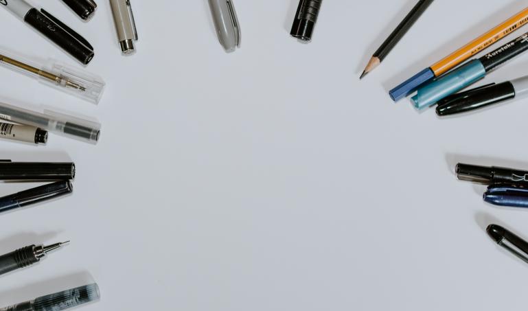 Pens and pencils arranged in a circle, surrounding a blank space.