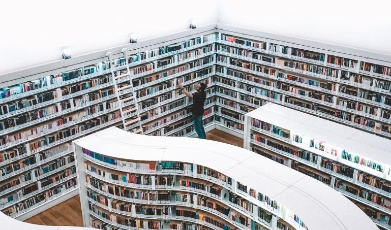 White bookshelves full of books and a man pulling a book off a far shelf