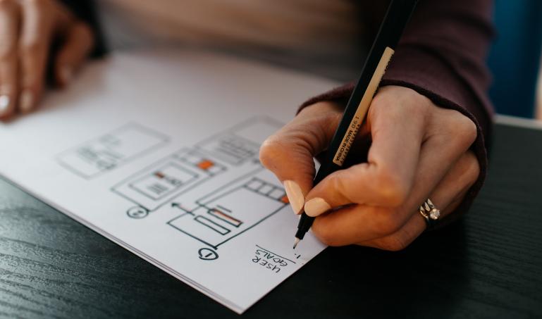 A hand writing on paper with UX wireframes