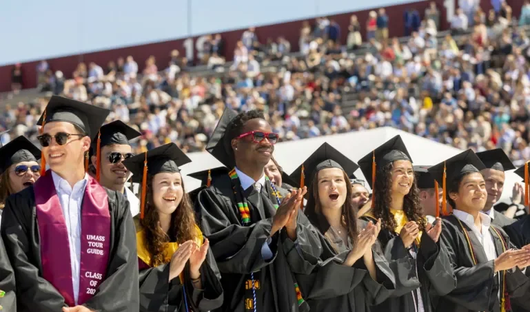 UMass Amherst students at graduation wearing caps and gowns.