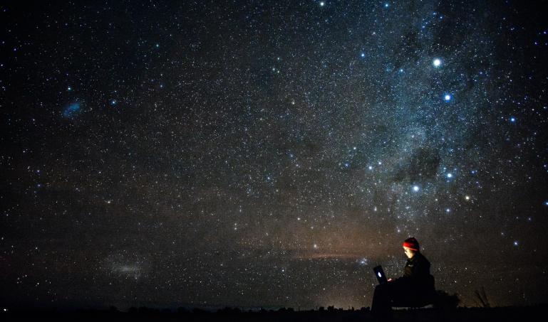 A person with a laptop in a remote location under a starry sky.