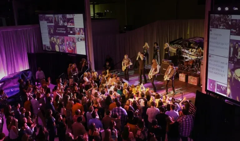 A crowd watches a rock concert with projected social media screens on either side of the stage