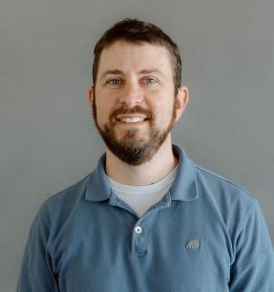 Adam Varn wearing a teal polo shirt in front of a gray background.