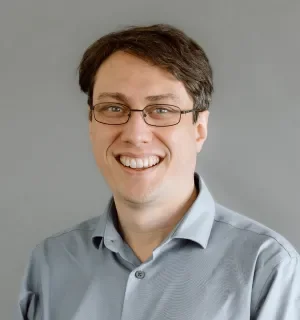 Photo of Andrew Berry, white male wearing a blue button down oxford shirt in front of a gray background.