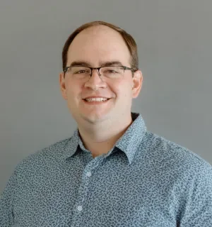 Andy Blum wearing a blue polo shirt in front of gray background.