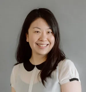 Betty Tran wearing a white blouse with black collar in front of a gray background.