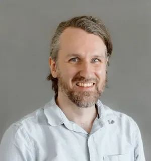 Danny Joris wearing a blue button down shirt in front of a gray background.