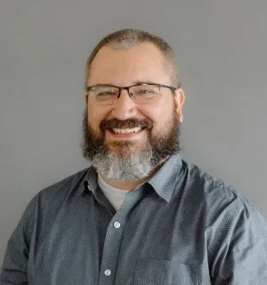 Darren Petersen wearing a blue button down shirt with white polka dots in front of a gray background