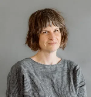 Frances Duncan wearing a black and white striped top in front of a gray backgound.